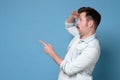 Young man pointing, surprised by something or someone, isolated on blue background.