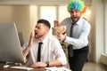 Young man popping paper bag behind his colleague in office. Funny joke