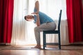 Young man practicing yoga using chair, doing Revolved Chair Pose Royalty Free Stock Photo