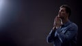 Young man praying in dark room under blessed light from heaven, Christianity