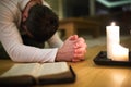 Young man praying, kneeling, Bible and candle next to him.