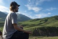Young man preforms yoga in mountains, Explorer look in summer mountain breathing fresh air, teenager in headphones listening music