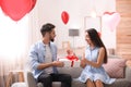 Young man presenting gift to his girlfriend in room decorated with heart shaped balloons. Valentine`s day celebration Royalty Free Stock Photo