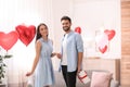 Young man presenting gift to his girlfriend in room decorated with heart shaped balloons. Valentine`s day celebration Royalty Free Stock Photo