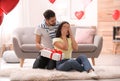 Young man presenting gift to his girlfriend in room decorated with heart shaped balloons. Valentine`s day celebration Royalty Free Stock Photo