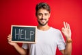 Young man with problem holding blackboard with help message over red bakground doing ok sign with fingers, excellent symbol