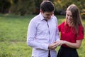 Young man proposing to his girlfriend outdoors in the park, putting the engagement ring on her finger