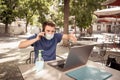 Young man with protective face mask on phone working outdoors remotely on computer