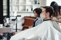 Young man in protective mask sitting in client chair at barber shop, waiting for haircut