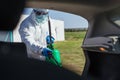 Man in protective suit with mask disinfecting inside car.