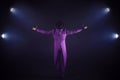 Young man in purple suit standing on the background of the spotlight. Showman spreading hands, show begins