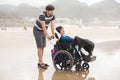 Young man pushing disabled little boy in wheelchair on beach Royalty Free Stock Photo