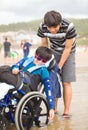 Young man pushing disabled little boy in wheelchair on beach Royalty Free Stock Photo