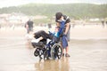 Young man pushing disabled little boy in wheelchair on beach Royalty Free Stock Photo