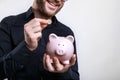 Young man putting coins in piggy bank. Saving for a rainy day Royalty Free Stock Photo