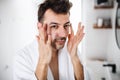 Young man putting cream on face in the bathroom in the morning, daily routine.