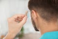 Young man putting hearing aid in ear indoors Royalty Free Stock Photo