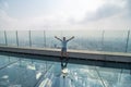 Young man with raised haands on a glass floor on the roof of a King Power Mahanakhon building