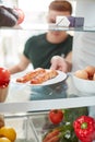 Young Man Reaching Inside Refrigerator Of Healthy Food For Fresh Salmon On Plate