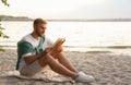 Young man reading book on sandy beach near sea Royalty Free Stock Photo