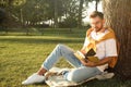 Young man reading book on green grass near tree in park Royalty Free Stock Photo