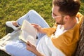 Young man reading book on green grass near tree in park Royalty Free Stock Photo