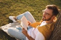 Young man reading book on green grass near tree in park Royalty Free Stock Photo