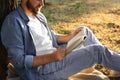 Young man reading book on green grass near tree in park, closeup Royalty Free Stock Photo