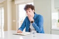 Young man reading a book at home cover mouth with hand shocked with shame for mistake, expression of fear, scared in silence,