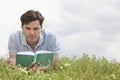 Young man reading book while lying on grass against sky Royalty Free Stock Photo
