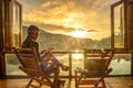 Young man reading book near window and watching lake view at coffee shop in the morning sunrise, Ban Rak Thai village, Mae Hong