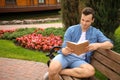 Young man reading book while sitting on wooden bench in park Royalty Free Stock Photo