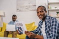 young man reading business newspaper and smiling at camera while senior father using Royalty Free Stock Photo