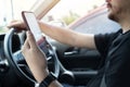 Young man reading messages holding a cell phone while driving. Dangerous behavior, accident risk