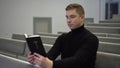 A young man reads the Bible while sitting on a church bench. A Protestant man reads the Bible in church. Royalty Free Stock Photo