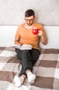 Young man reads a book in bed and drinks coffee. Vertical photo