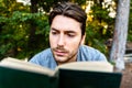 Young man reads a self-absorbed novel sitting in a park at sunset, enjoying ancient literature