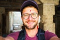 Young man with red bindi dot wearing glasses cap and a backpack posing for a selfie Royalty Free Stock Photo