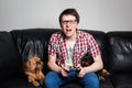 A young man in a red shirt and blue jeans sits at home and plays video games together with their dog. Screaming boy in front of tv