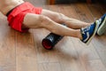 A young man in red shorts is doing exercises on a foam roller, works out of the muscles with a massage roller. Athletic