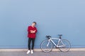 Young man in a red sweatshirt standing by a bicycle on a blue background and looking at the camera Royalty Free Stock Photo