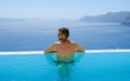 young man relaxing in swimming pool during vacation at Santorini infinity looking out over the ocean