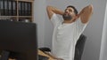 Young man relaxing in a modern office with files in the background, appearing calm and content at his workstation Royalty Free Stock Photo