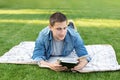 Young man relaxing and reading book while lying on lawn. Happy Man Lying On Green Grass and study remotely. Royalty Free Stock Photo