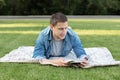 Young man relaxing and reading book while lying on lawn. Happy Man Lying On Green Grass and study remotely. Royalty Free Stock Photo