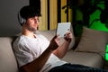 Young man relaxing on sofa in his living room. he is listening to a music on headphones and using digital tablet Royalty Free Stock Photo