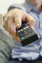 Young man relaxing on sofa and holding TV remote control. the TV remote is in foreground. Switching channels. vertical photo Royalty Free Stock Photo