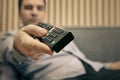 Young man relaxing on sofa and holding TV remote control. the TV remote is in foreground. Switching channels Royalty Free Stock Photo