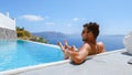 young man relaxing in swimming pool during vacation at Santorini infinity looking out over the ocean