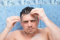 Young man is removing alginate mask from his face lying in bathroom with foam.